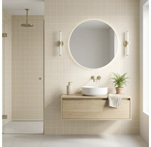 Modernes Badezimmer mit schwebendem Waschtischunterschrank aus Holz, weißem Aufsatzbecken, beleuchtetem Rundspiegel und beigen Fliesen.
