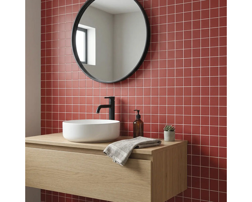 Modernes Badezimmer mit roten Mosaikfliesen, rundem Spiegel, hölzernem Waschtischunterschrank, weißem Aufsatzwaschbecken und schwarzer Armatur.