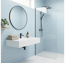 Modernes Badezimmer mit hellblauen Fliesen, weißem Waschtisch, schwarzer Armatur, rundem Spiegel und begehbarer Dusche mit Glastrennwand.