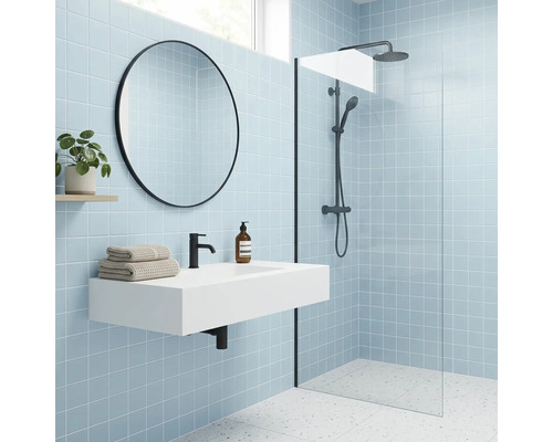 Modernes Badezimmer mit hellblauen Fliesen, weißem Waschtisch, schwarzer Armatur, rundem Spiegel und begehbarer Dusche mit Glastrennwand.