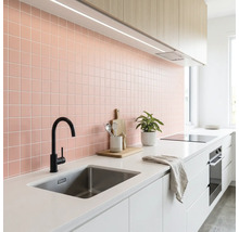 Moderne helle Küche mit rosa Fliesenspiegel, weißer Arbeitsplatte, Edelstahlspüle, schwarzer Armatur und Holzschränken.