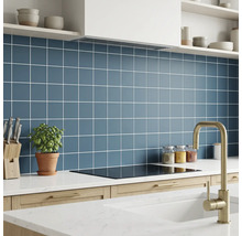 Moderne Küche mit quadratischen blauen Wandfliesen, weißen Fugen, weißer Arbeitsplatte, Induktionskochfeld und goldfarbenem Wasserhahn.