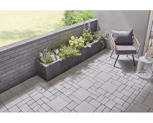 Moderne Terrasse mit Pflastersteinen, Gartenmauer aus Betonsteinen und einem bepflanzten Pflanzkasten.