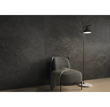 Dunkle Wandfliesen in Natursteinoptik in einem modern eingerichteten Wohnzimmer mit grauem Sessel und minimalistischer Stehlampe.