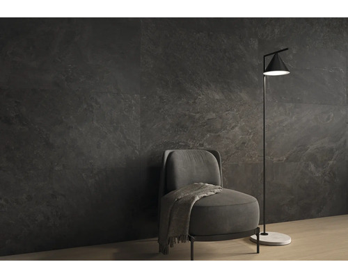 Dunkle Wandfliesen in Natursteinoptik in einem modern eingerichteten Wohnzimmer mit grauem Sessel und minimalistischer Stehlampe.