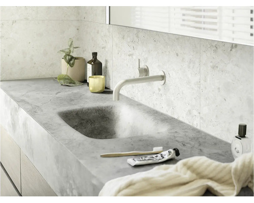 Modernes Badezimmer mit integriertem Naturstein-Waschbecken, wandmontierter Armatur und hellen Terrazzo-Wandfliesen.