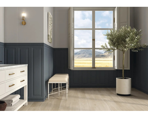 Heller Raum mit blauer Wandtäfelung, Fenster mit Bergblick, hellem Holzboden, weißem Waschtisch und Olivenbaum im Topf.