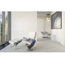 Hell gestalteter Wohnraum mit großformatigen Wand- und Bodenfliesen, modernem Designer-Sessel mit Fußhocker und minimalistischer Einrichtung.