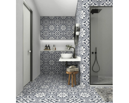 Modernes Badezimmer mit gemusterten Zementfliesen an Boden und Wänden, weißem Aufsatzwaschbecken und einer begehbaren Dusche mit schwarzen Armaturen.