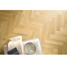 Laminatboden mit klassischem Fischgrätmuster in Holzoptik, verlegt in einem Wohnraum mit Polsterhocker, Decke und dekorativen Accessoires.