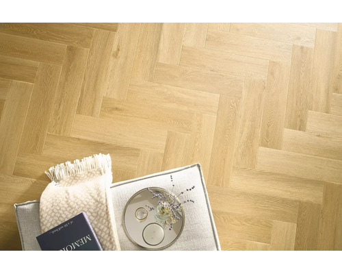 Laminatboden mit klassischem Fischgrätmuster in Holzoptik, verlegt in einem Wohnraum mit Polsterhocker, Decke und dekorativen Accessoires.