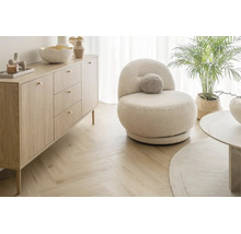 Helles Wohnzimmer mit einem beigen runden Sessel, einer Sideboard Kommode aus Holz und Fischgrätparkett.