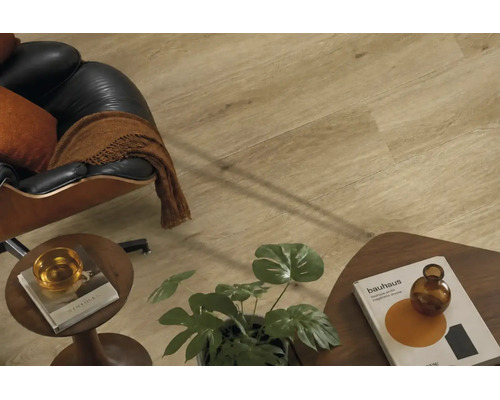 Wohnraum mit Laminatboden in Holzoptik, dazu ein Sessel aus Leder und Holztischen mit Dekoration in einem modern eingerichteten Zimmer.