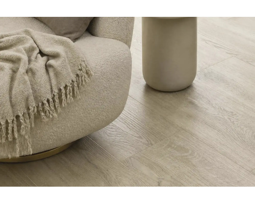 Heller Laminatboden mit natürlicher Holzoptik verlegt in einem Wohnbereich mit modernem Sessel und Beistelltisch.