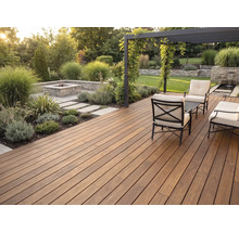 Moderne Holzterrasse mit dunklen Dielen, Sitzgruppe aus Metall, hellen Polstern, Pergola und gemauerter Feuerstelle im gepflegten Garten.