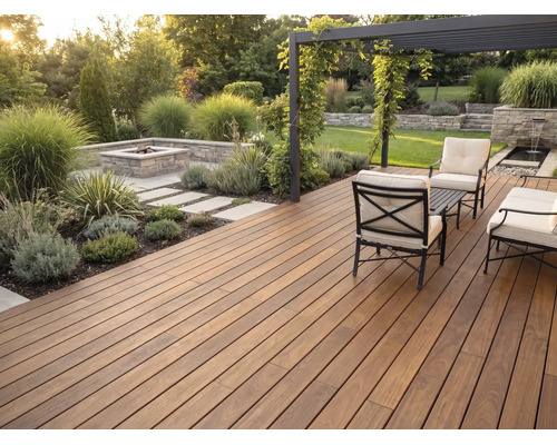 Moderne Holzterrasse mit dunklen Dielen, Sitzgruppe aus Metall, hellen Polstern, Pergola und gemauerter Feuerstelle im gepflegten Garten.