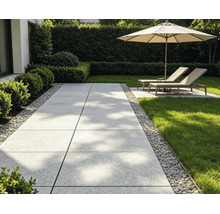 Moderner Gartenweg aus großen grauen Terrassenplatten mit Kiesumrandung, angrenzendem Rasen und Liegestühlen unter einem Sonnenschirm.