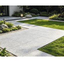 Modern gestaltete Garten-Terrasse mit hellen, großformatigen Gehwegplatten, angrenzendem Rasen und gepflegten Beeten mit Kies.