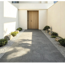 Moderner Eingangsbereich mit einem Gehweg aus großen grauen Terrassenplatten, gesäumt von weißem Kies, kleinen Sträuchern und Steinen.
