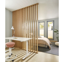 Moderne Raumtrennung durch vertikale Holzlamellen zwischen Arbeitsplatz mit Schreibtisch und Schlafbereich in einem hellen, offenen Wohnraum.