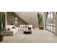 Geräumiges Wohnzimmer mit Steinfliesenboden, modernen Polstermöbeln, offener Holztreppe und großen Kakteen in einem hellen, naturnahen Interieur.