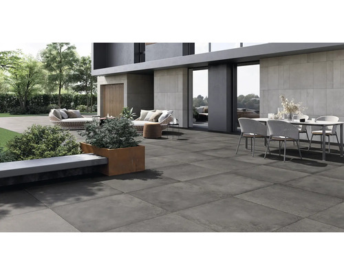 Moderne Terrassenplatte aus Feinsteinzeug auf einer weitläufigen Außenterrasse mit Gartenmöbeln vor einem modernen Wohnhaus.