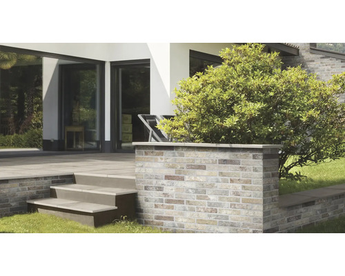 Moderne Terrasse mit einer Mauer aus Klinkerriemchen und einer Treppe aus Steinplatten vor einem hellen Wohnhaus mit grossen Fensterfronten.