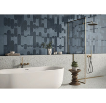 Modernes Badezimmer mit gemusterten Wandfliesen, Terrazzooptik im unteren Bereich, freistehender Badewanne und goldfarbener Duscharmatur.