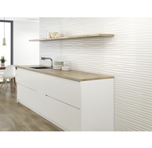 Küchenszene mit weißen Unterschränken, einer Holzablage und einer Wand mit gewellter Fliesenstruktur.