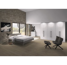 Helles Schlafzimmer mit Bett, großem Schrank, Sessel und Fußhocker