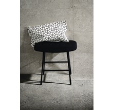 Dekoratives Kissen auf einem schwarzen Hocker vor Fliesenwand