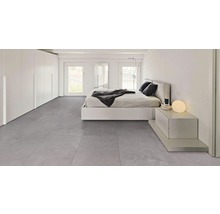 Heller Schlafraum mit Bett, Kommode, Fenster und grauem Fliesenboden.