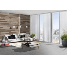 Wohnzimmer mit grauer Couch, Ottomanen, Holzvertäfelung und weißen Lamellenvorhängen an großen Fenstern.