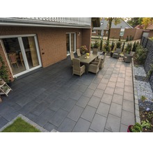 Terrasse mit Steinfliesen, Gartentisch und Stühlen vor einem Haus