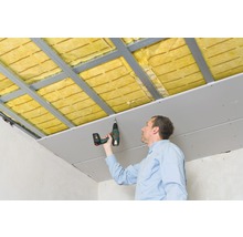 Mann befestigt eine Gipskartonplatte mit einem Akkuschrauber an einer Deckenkonstruktion mit Dämmmaterial.