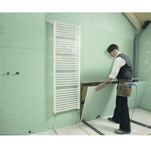 Ein Handwerker montiert eine Gipskartonplatte in einem Badezimmer mit Heizkörper.