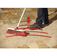 Eine Person kehrt Fugensand mit einem Straßenbesen in die Pflasterfugen ein.