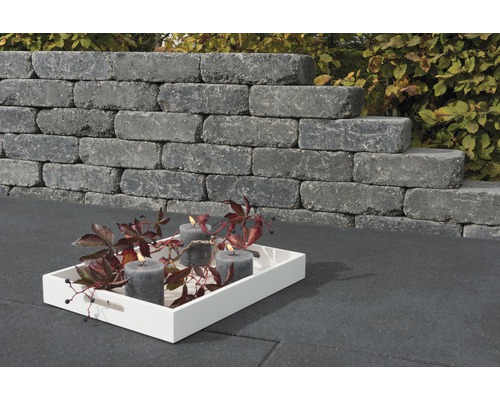 Gestapelte Mauersteine mit Kerzen auf Tablett im Garten.