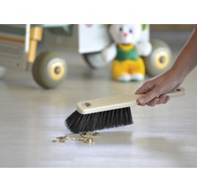 Handfeger mit Holzgriff und dunklen Borsten kehrt Krümel vom Boden.