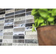 Detailaufnahme einer Wand mit Mosaikfliesen in verschiedenen Grautönen, neben einer Pflanze