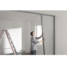 Mann montiert Trockenbauwand mit Metallprofilen in einem Raum.