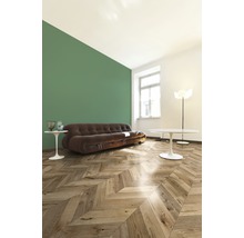 Wohnzimmer mit braunem Sofa, Holzboden im Fischgrätmuster und grüner Wand