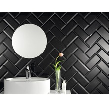 Badezimmer mit schwarzem Fischgrätenfliesenmuster, Waschbecken und rundem Spiegel