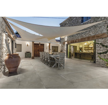 Außenbereich mit Steintisch, Stühlen und Bodenfliesen unter einem Sonnensegel.