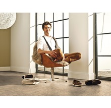 Ein Mann sitzt entspannt in einem Sessel in einem hellen Raum mit großem Fenster und Bodenbelag.