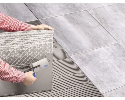 Fliesenleger legt Fliesen mit einer Fliesenkelle auf einem Untergrund