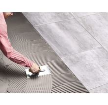 Ein Mann verlegt Fliesen mit einem Spachtel, um Fliesenkleber zu verteilen