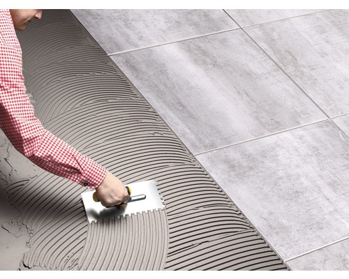 Ein Mann verlegt Fliesen mit einem Spachtel, um Fliesenkleber zu verteilen