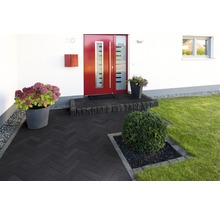 Eingangsbereich eines Hauses mit dunklen Pflastersteinen, Blumen und einem gepflegten Garten