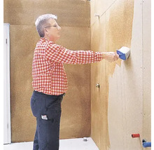 Mann trägt mit einer Bürste Beschichtung auf eine Wand auf